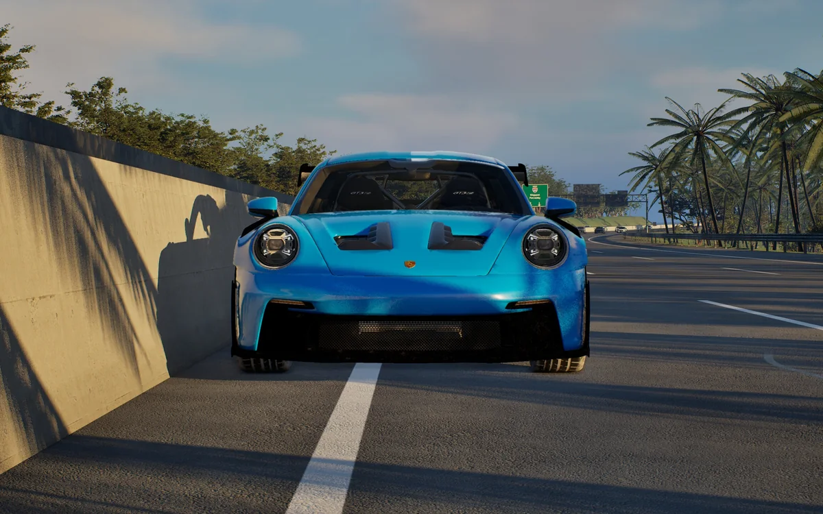 A blue sports car coming head-on down a palm-lined coastal highway at golden hour